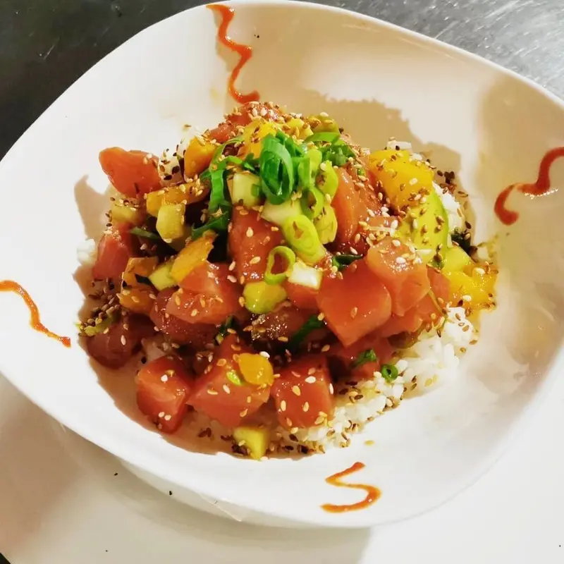 Poke de atún con aguacate, cebollino y ajonjolí sobre arroz, en un tazón blanco
