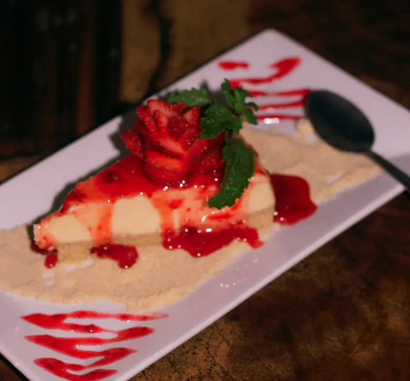 Cheesecake con salsa de fresa y hojas de menta sobre un plato rectangular