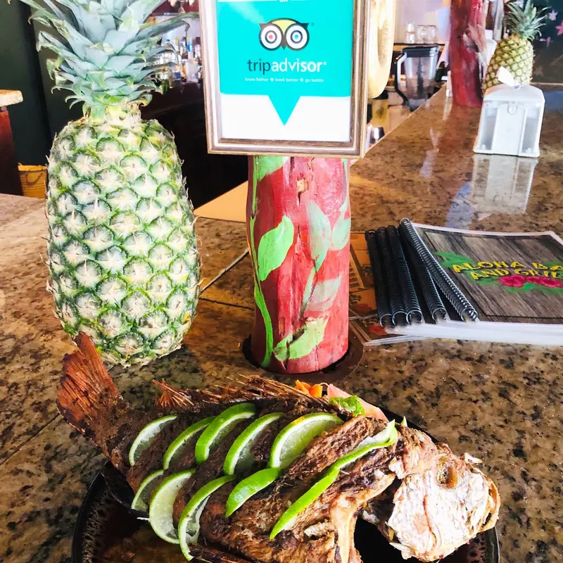 Pescado entero con rodajas de lima junto a una piña decorativa en la barra