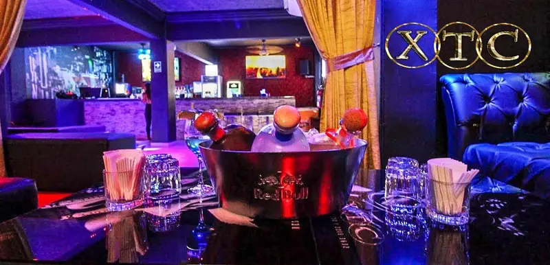 Salón con sofás azules, una hielera con botellas sobre la mesa y la barra al fondo