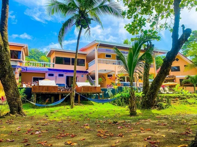 Edificio del hotel de varios pisos con habitaciones de colores frente a un jardín con palmeras