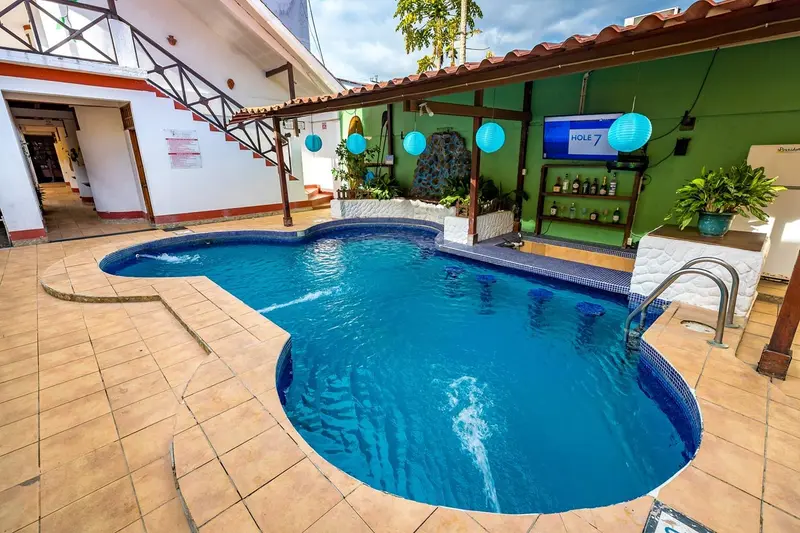 Piscina del hotel con la terraza del bar de paredes verdes y faroles azules al fondo