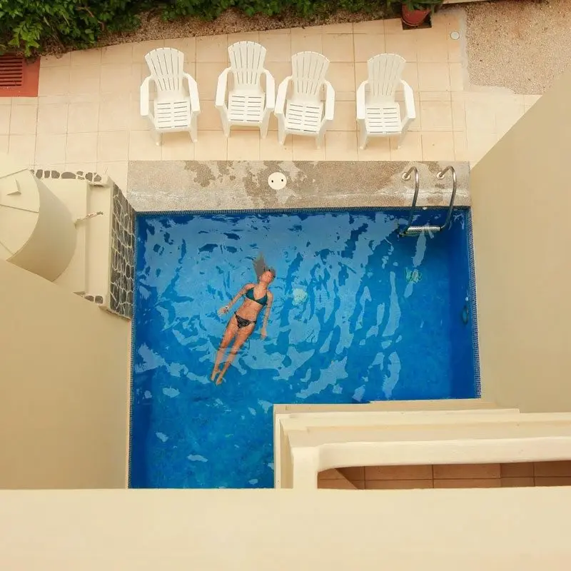 Piscina pequeña vista desde arriba, con cuatro sillas blancas al fondo