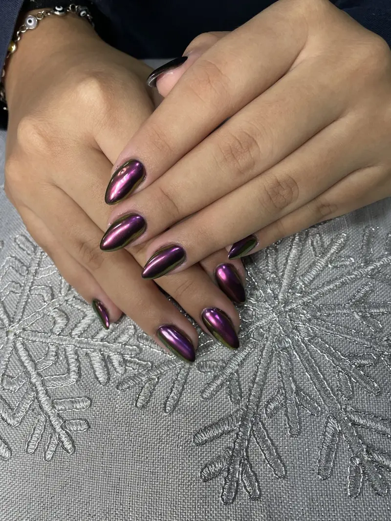 Manos con uñas largas en tono morado metálico sobre una tela gris