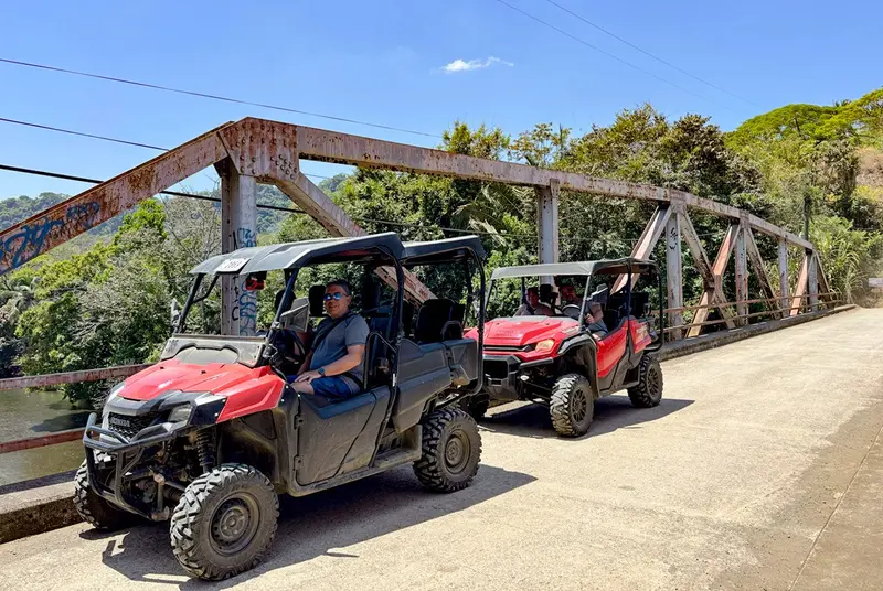 Dos buggies rojos cruzando un puente metálico de un carril sobre un camino de tierra