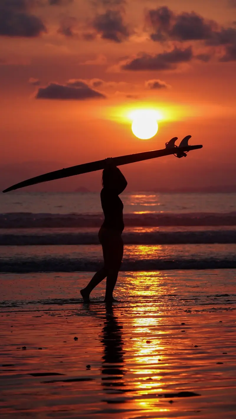 Silueta de una persona con la tabla sobre la cabeza frente a un atardecer naranja