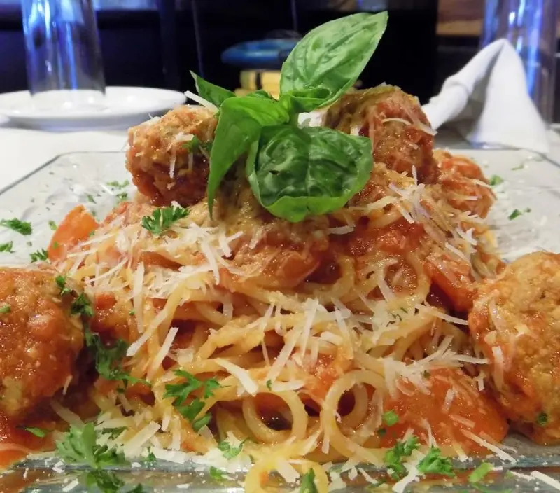 Espagueti con albóndigas en salsa de tomate, queso rallado y una hoja de albahaca