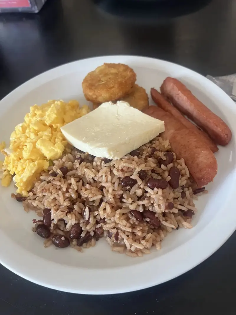 Desayuno con gallo pinto, huevos revueltos, queso blanco, salchichas y una tortita dorada