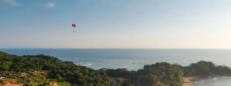 Parapente lejano sobre la costa y el mar al atardecer, con colinas verdes abajo