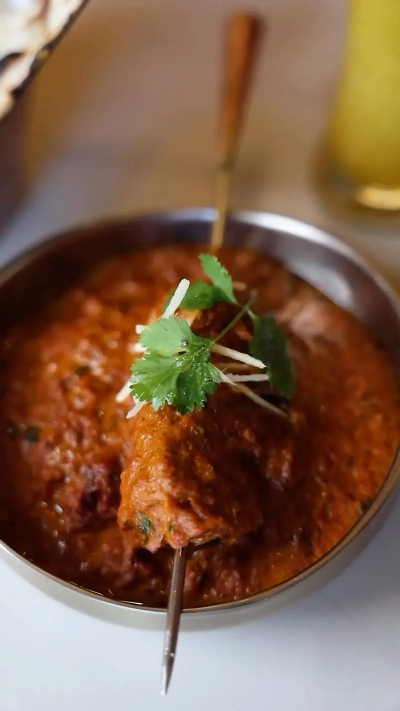 Curry rojo de carne con cilantro en un cuenco de metal, atravesado por una brocheta