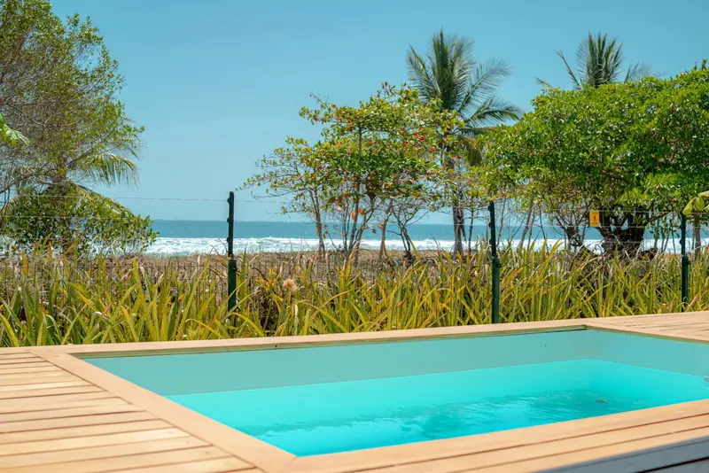 Piscina privada junto a la playa, con palmeras y el mar al fondo
