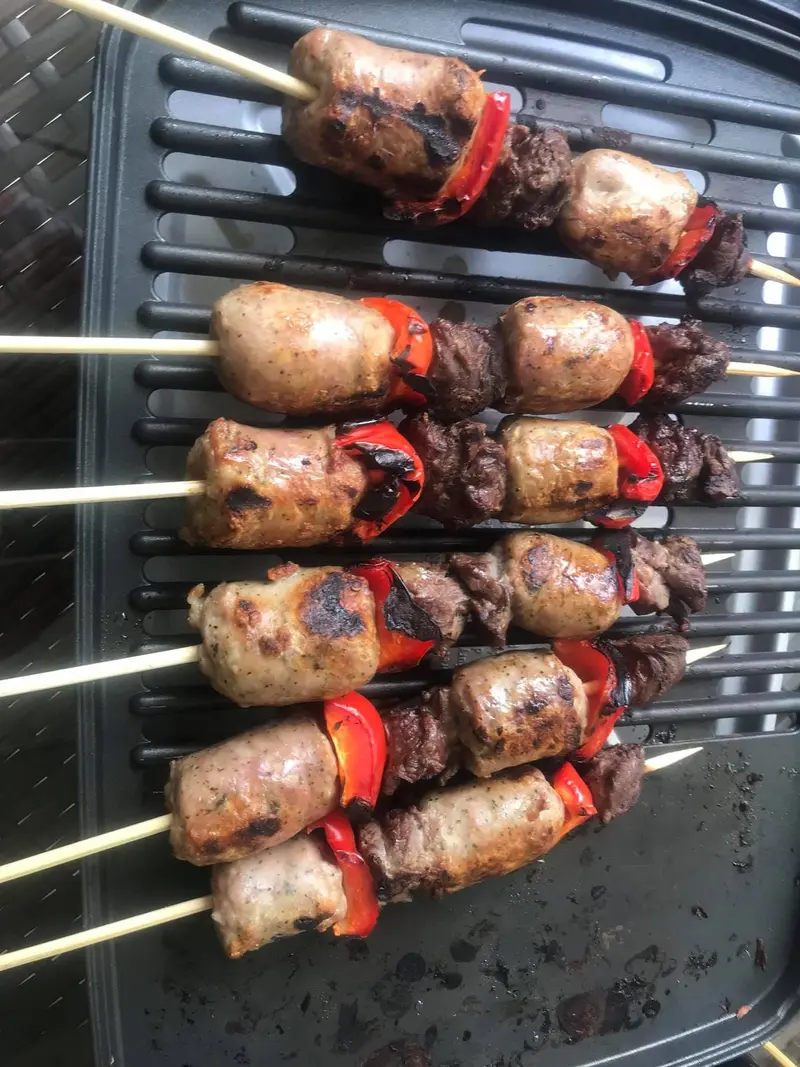 Brochetas de embutido, carne y pimiento rojo sobre una parrilla
