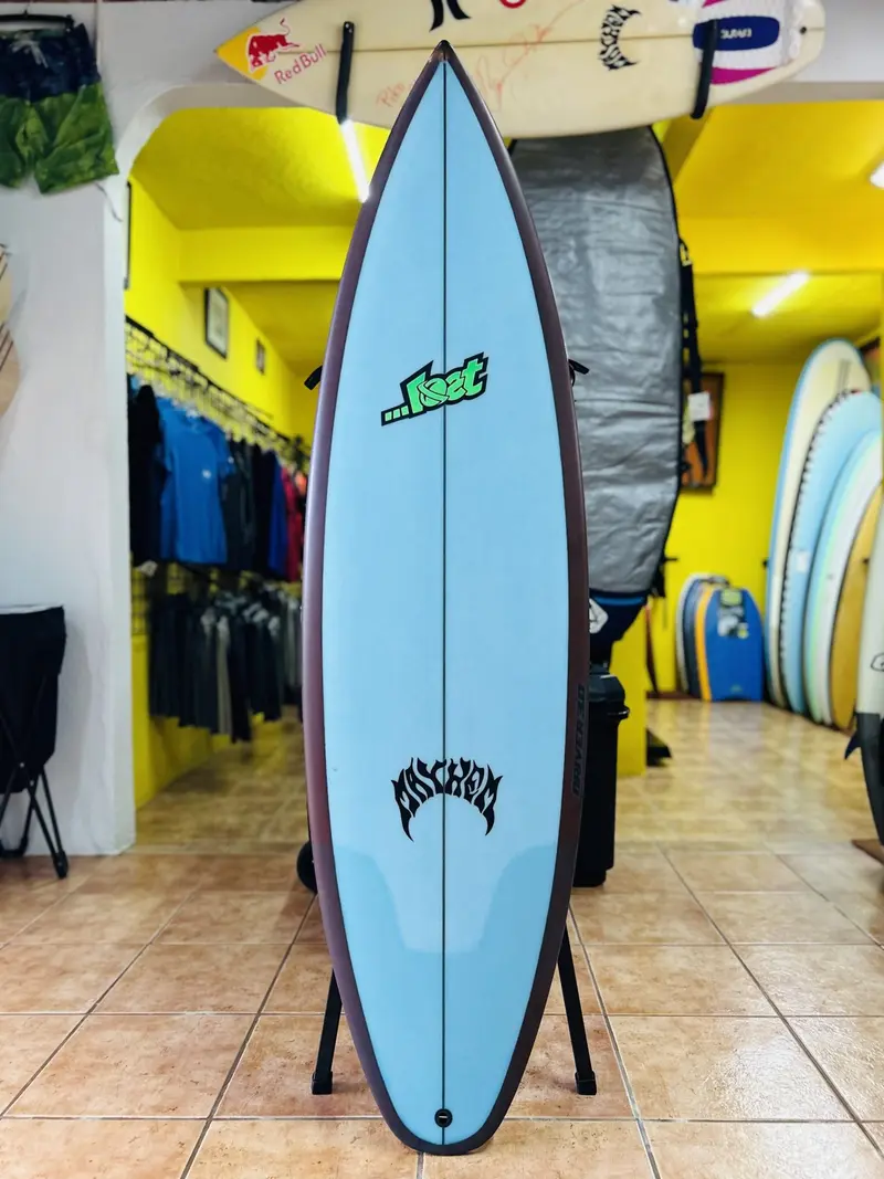 Tabla Lost celeste con bordes oscuros sobre un soporte, frente a la pared amarilla de la tienda