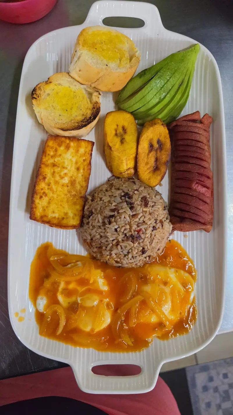 Plato largo con gallo pinto, huevos en salsa, queso frito, aguacate, plátano maduro, salchichón y pan con mantequilla