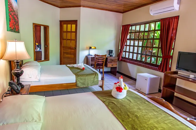 Habitación con dos camas con camino verde, escritorio con lámpara y ventana con marco de madera