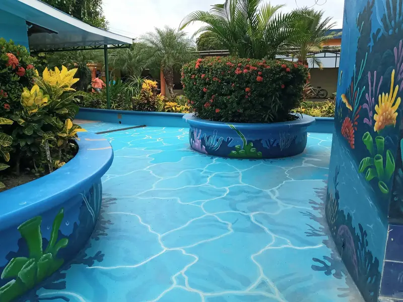 Piscina curva con una jardinera en el centro y un muro con mural azul