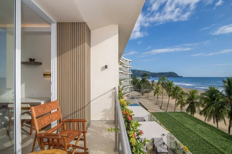 Balcón de una habitación con sillas de madera y vista a la playa y a la costa