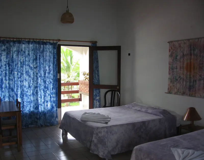 Habitación con cama matrimonial, cortinas azules y una puerta abierta al balcón