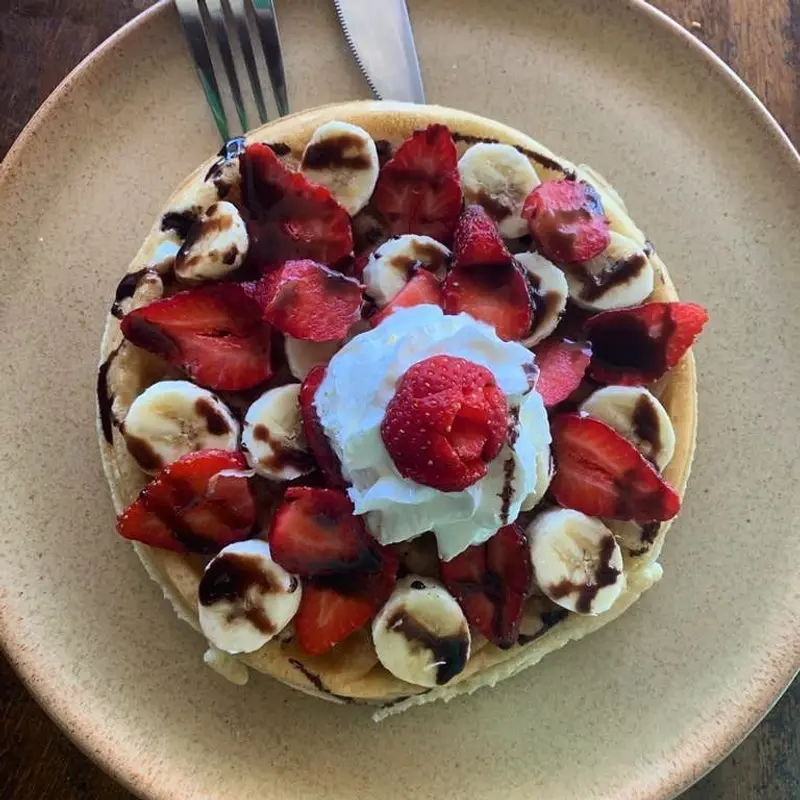 Pancakes con fresas, banano, crema chantillí y sirope sobre un plato
