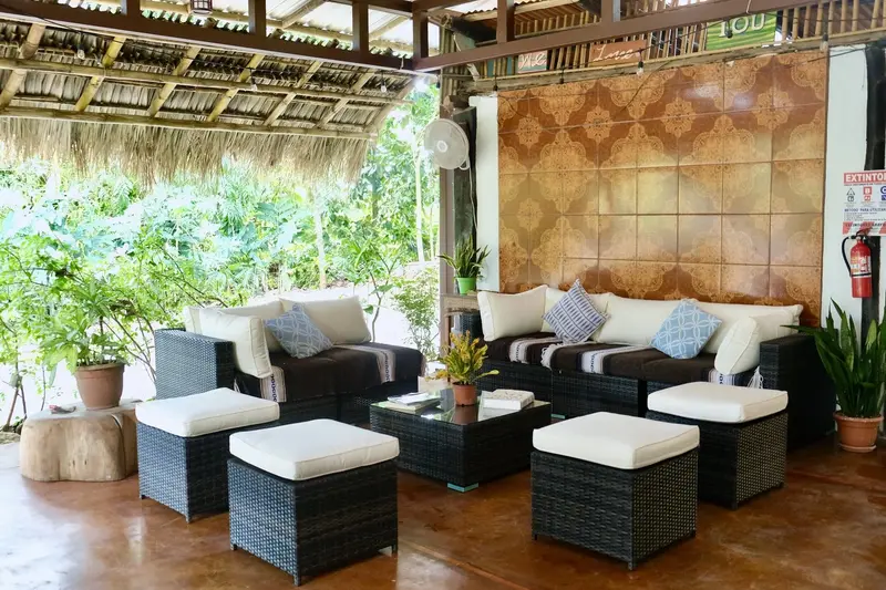 Sala de estar techada con sofás, pufs y plantas, abierta al jardín