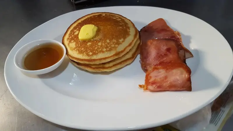 Desayuno con pancakes con mantequilla, miel y tocineta en un plato blanco