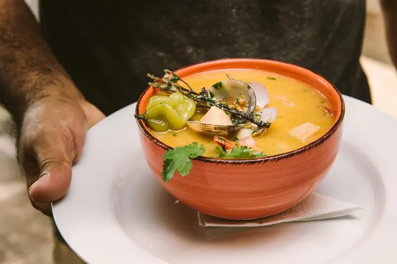 Sopa anaranjada con mariscos en un tazón sostenido sobre un plato blanco