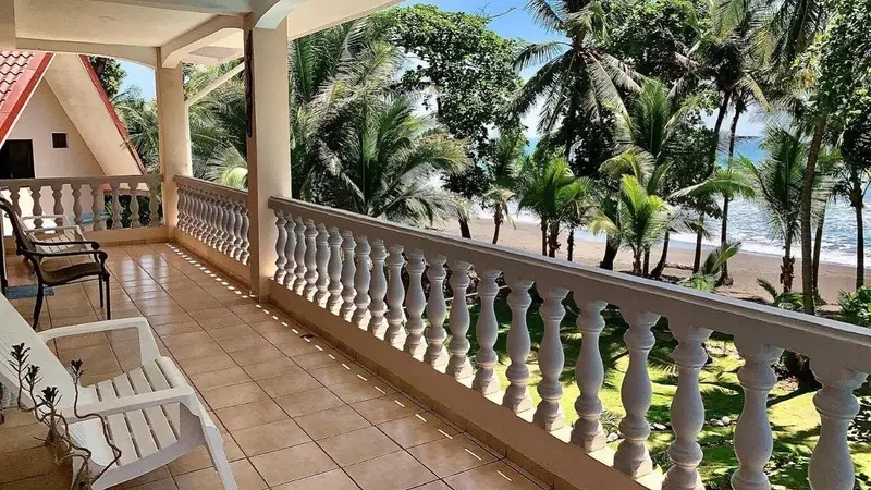 Balcón con baranda blanca y sillas, con palmeras y la playa al fondo