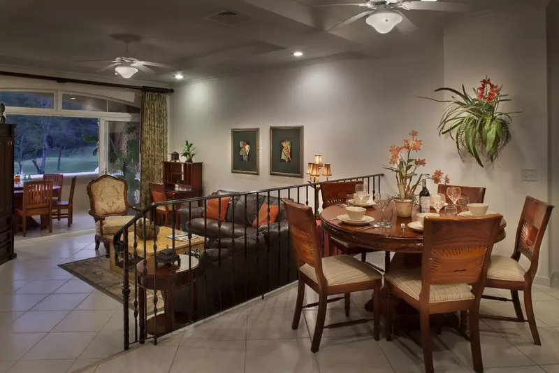 Sala y comedor de un apartamento, con mesa redonda de madera, sillones y ventanales hacia el verde