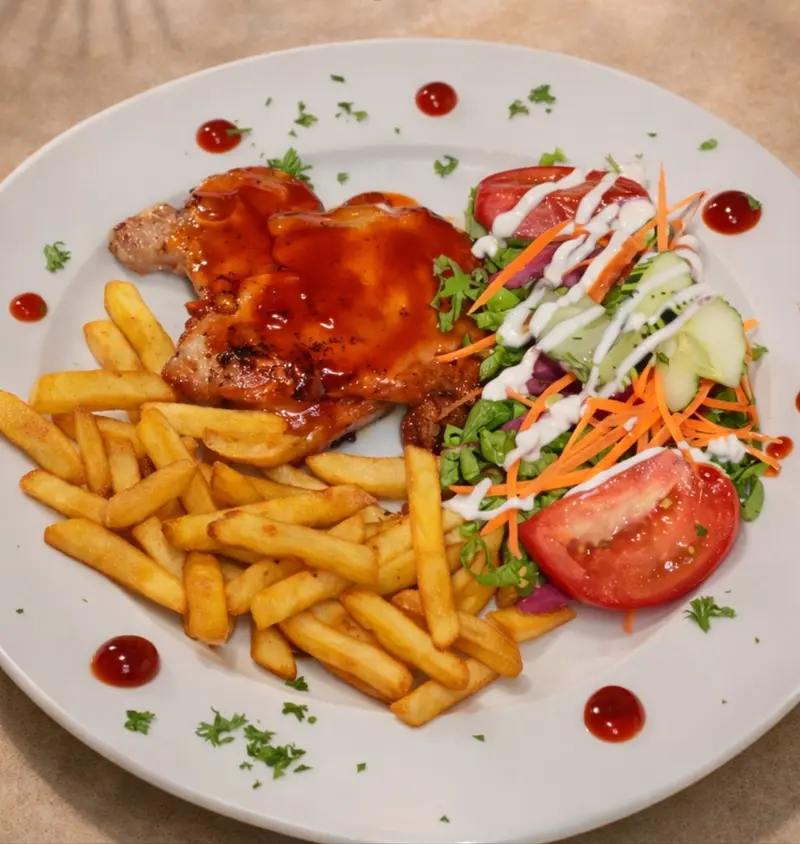Plato con chuleta bañada en salsa roja, papas fritas y ensalada con tomate y zanahoria