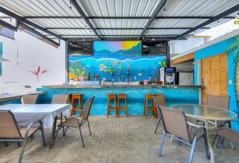 Terraza con mesas y sillas frente a una barra decorada con un mural azul de mar