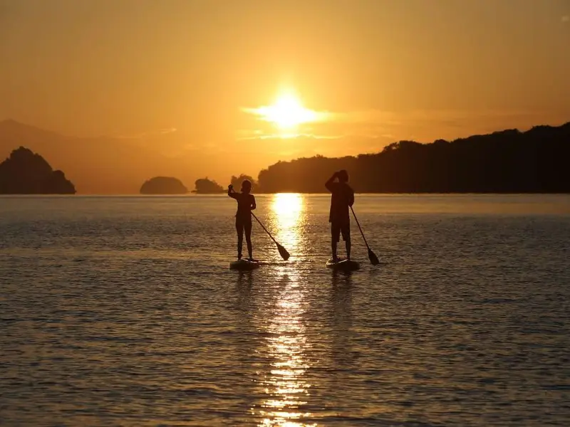 Dos personas remando al atardecer frente a la costa