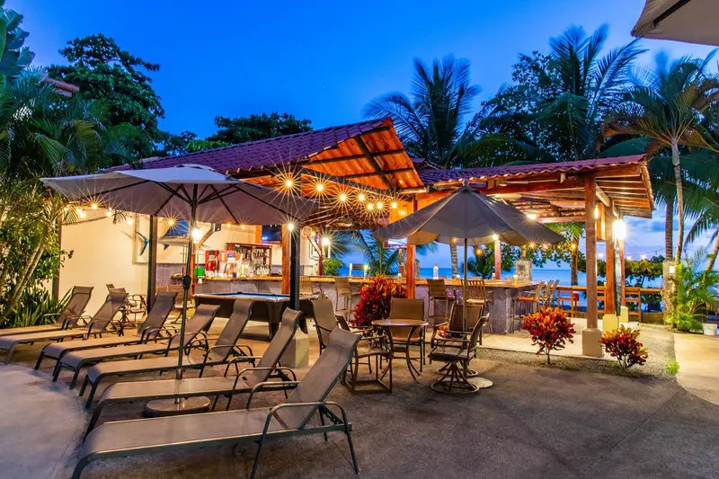 Restaurante y bar bajo techo de palma con sombrillas y camastros junto a la piscina, al atardecer