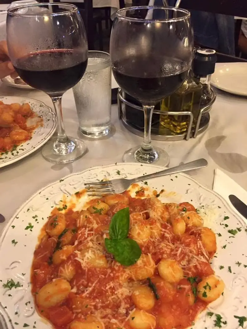 Ñoquis en salsa de tomate con albahaca y parmesano, junto a dos copas de vino tinto