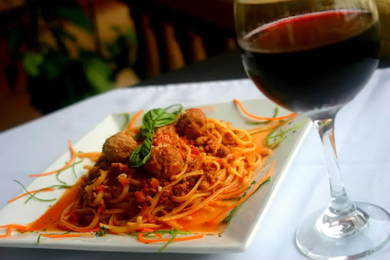 Espagueti con albóndigas y albahaca sobre un plato blanco, junto a una copa de vino tinto